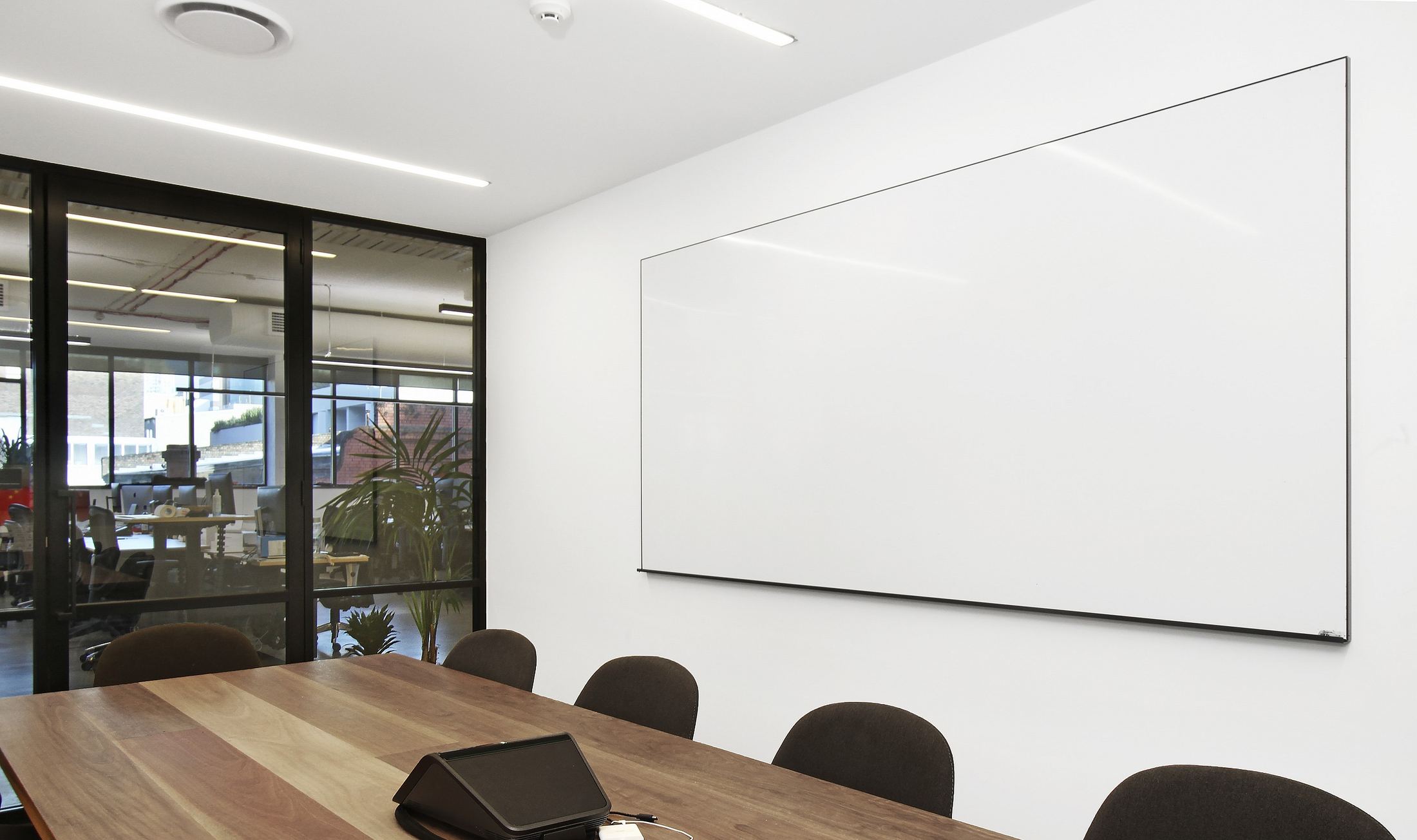 A large powdercoated frame whiteboard beside a glass-walled meeting room